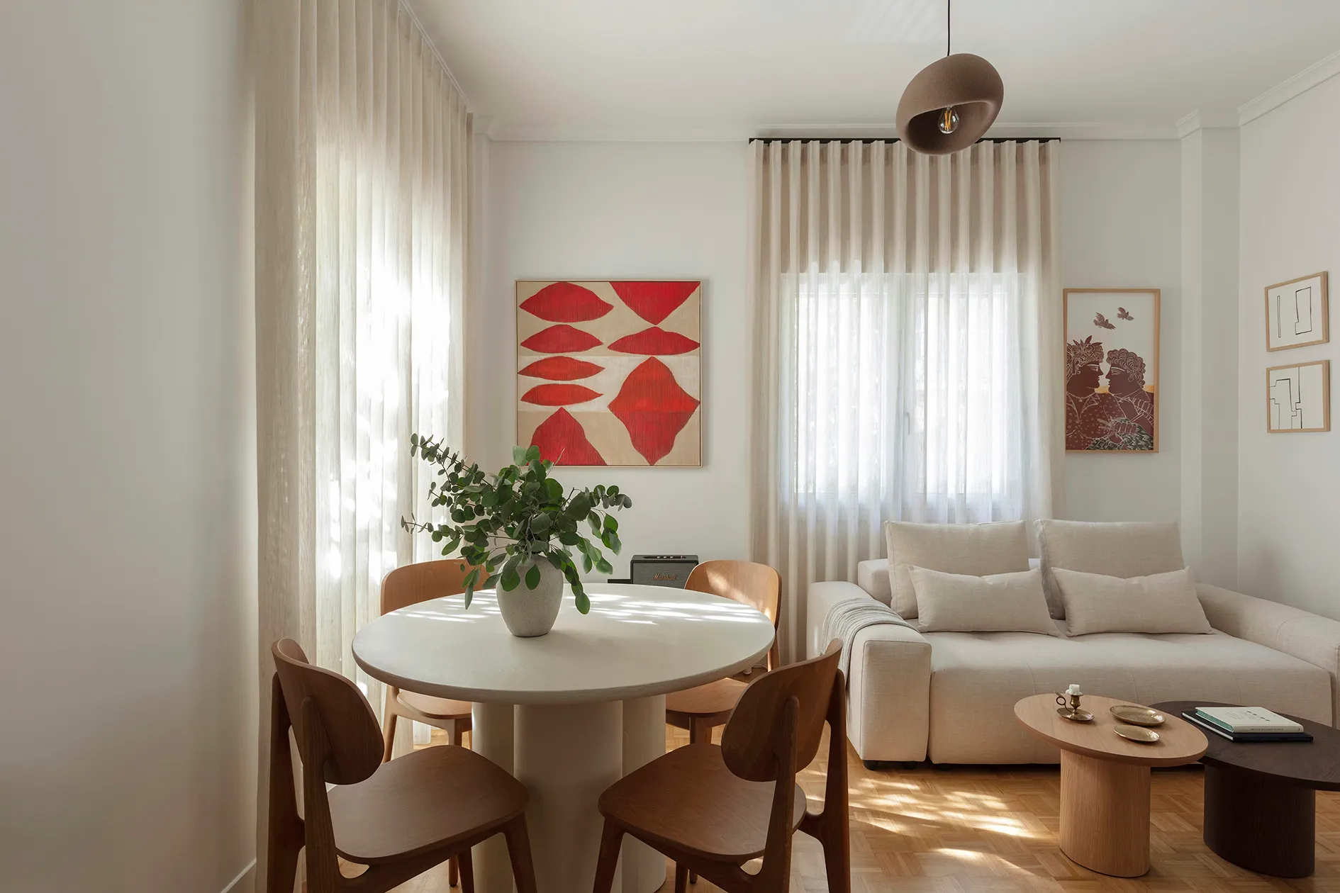 Dining table and living area surrounded by artwork and softly curtained windows