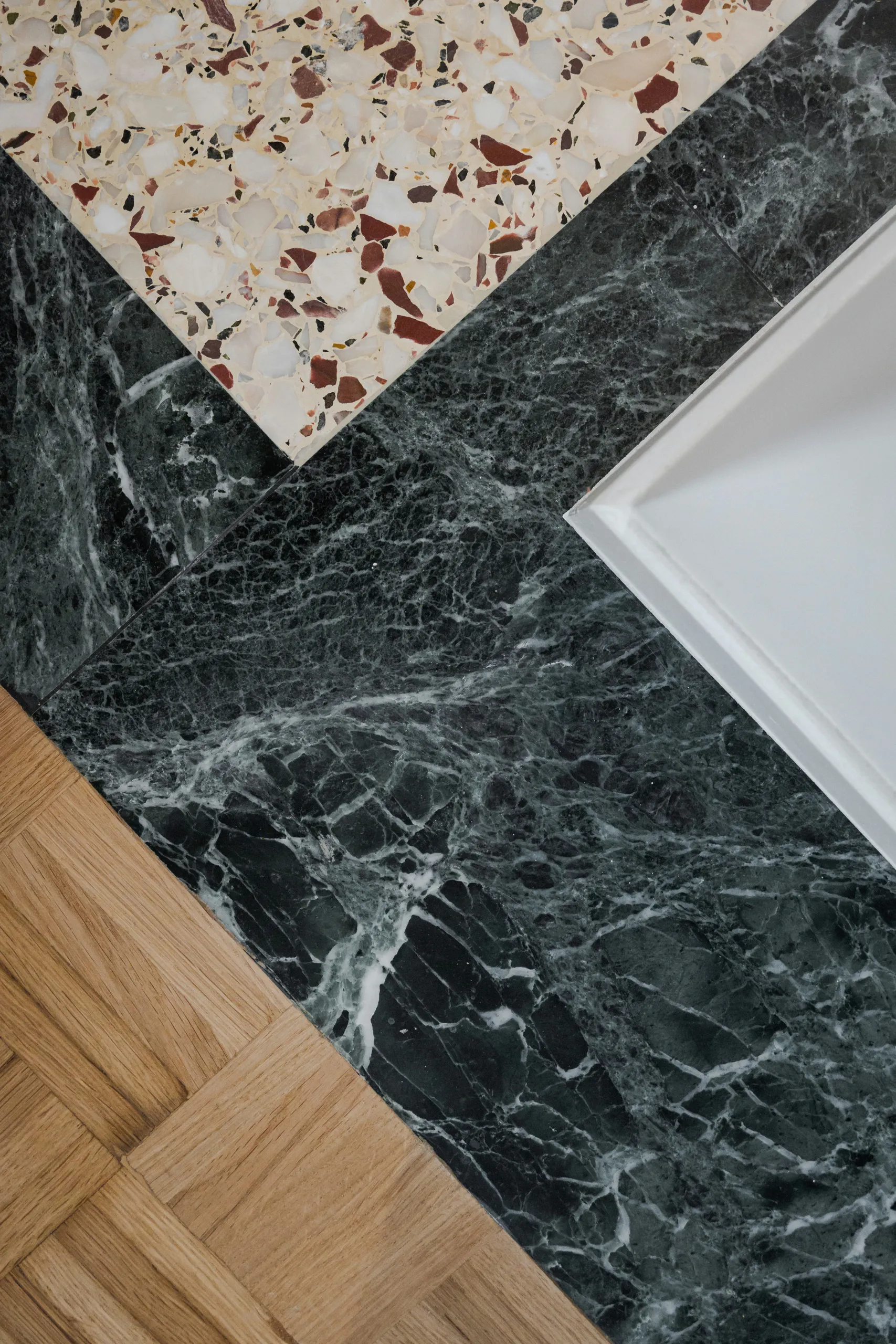 Junction of restored terrazzo, dark Tinos marble and oak parquet floors