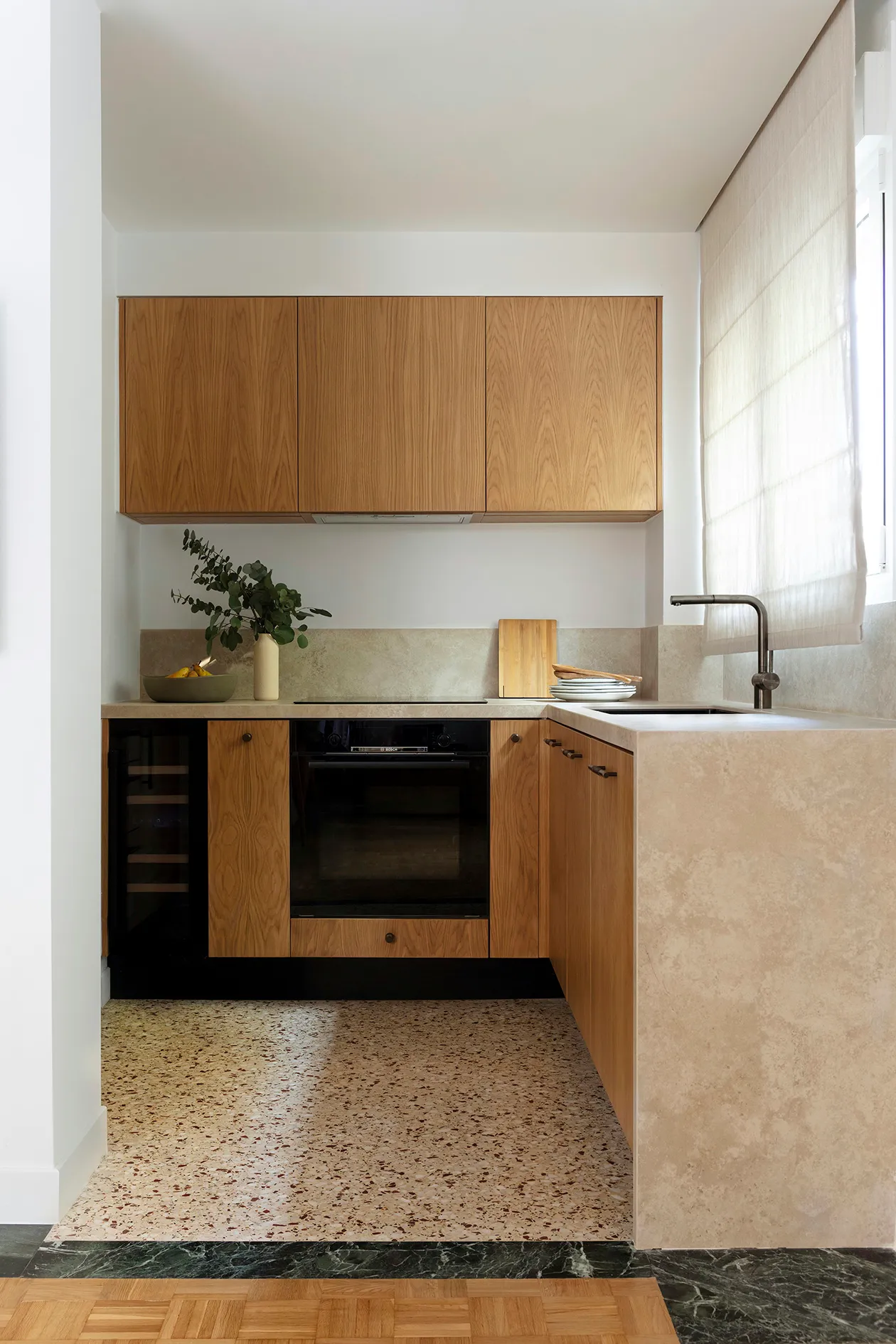 Compact kitchen with oak cabinetry, stone worktops and restored terrazzo floor