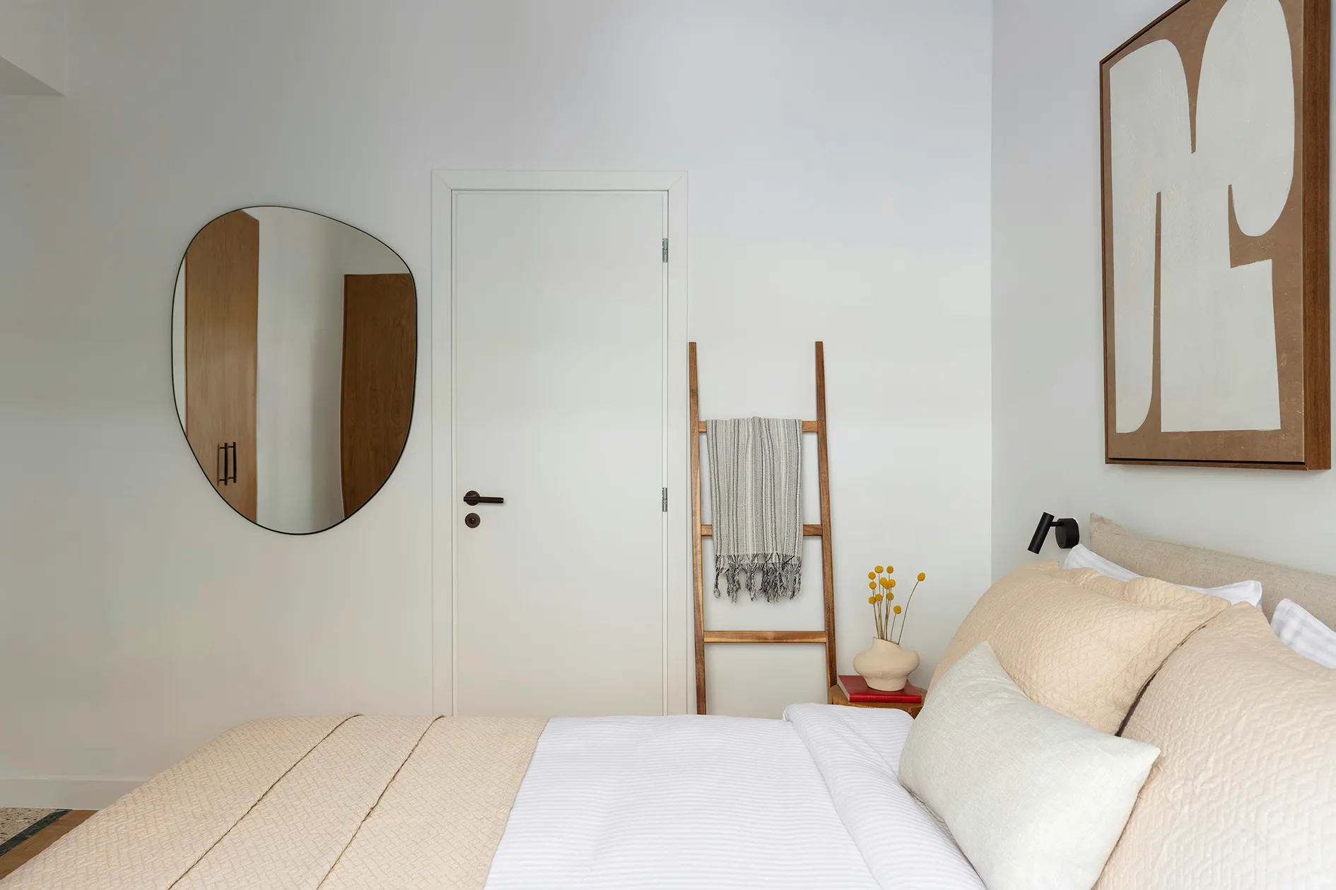 Bedroom with upholstered bed, round mirror and timber blanket ladder