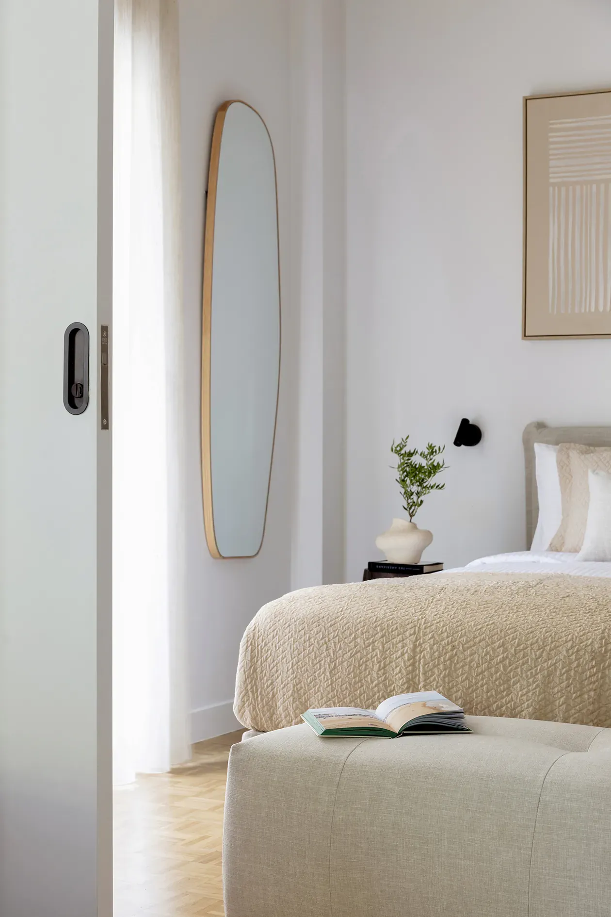 Bedroom viewed past the sliding door, with a full-height curved mirror