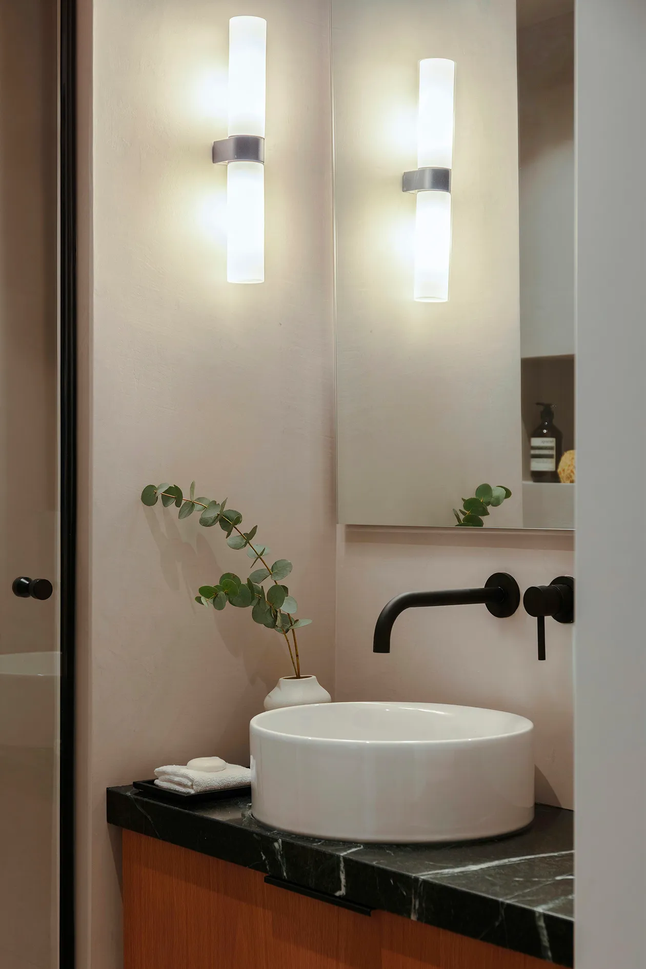Bathroom basin with dark marble worktop, black tap and illuminated mirror