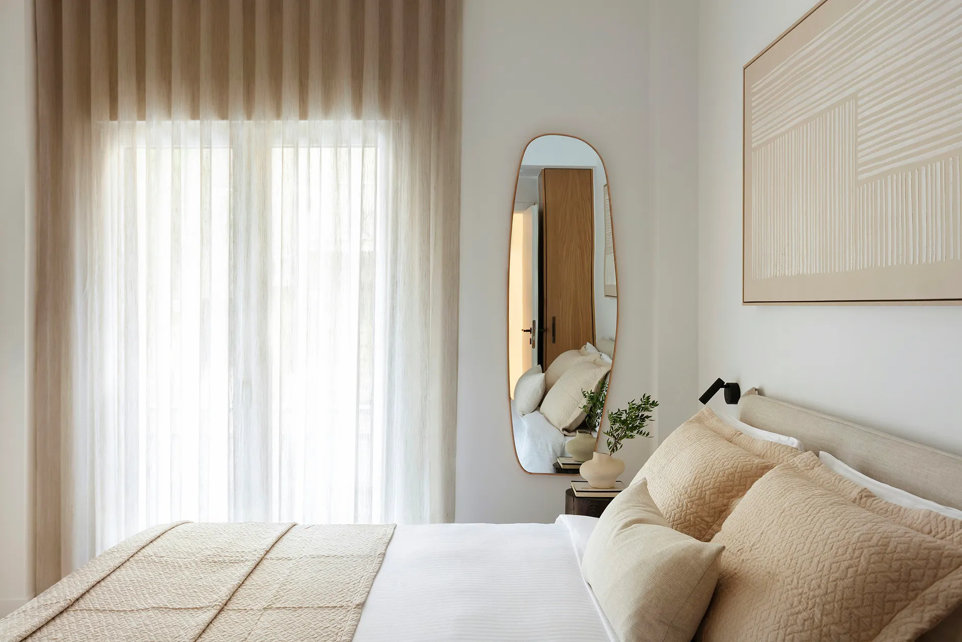 Bedroom with neutral textiles, curved mirror and softly filtered daylight